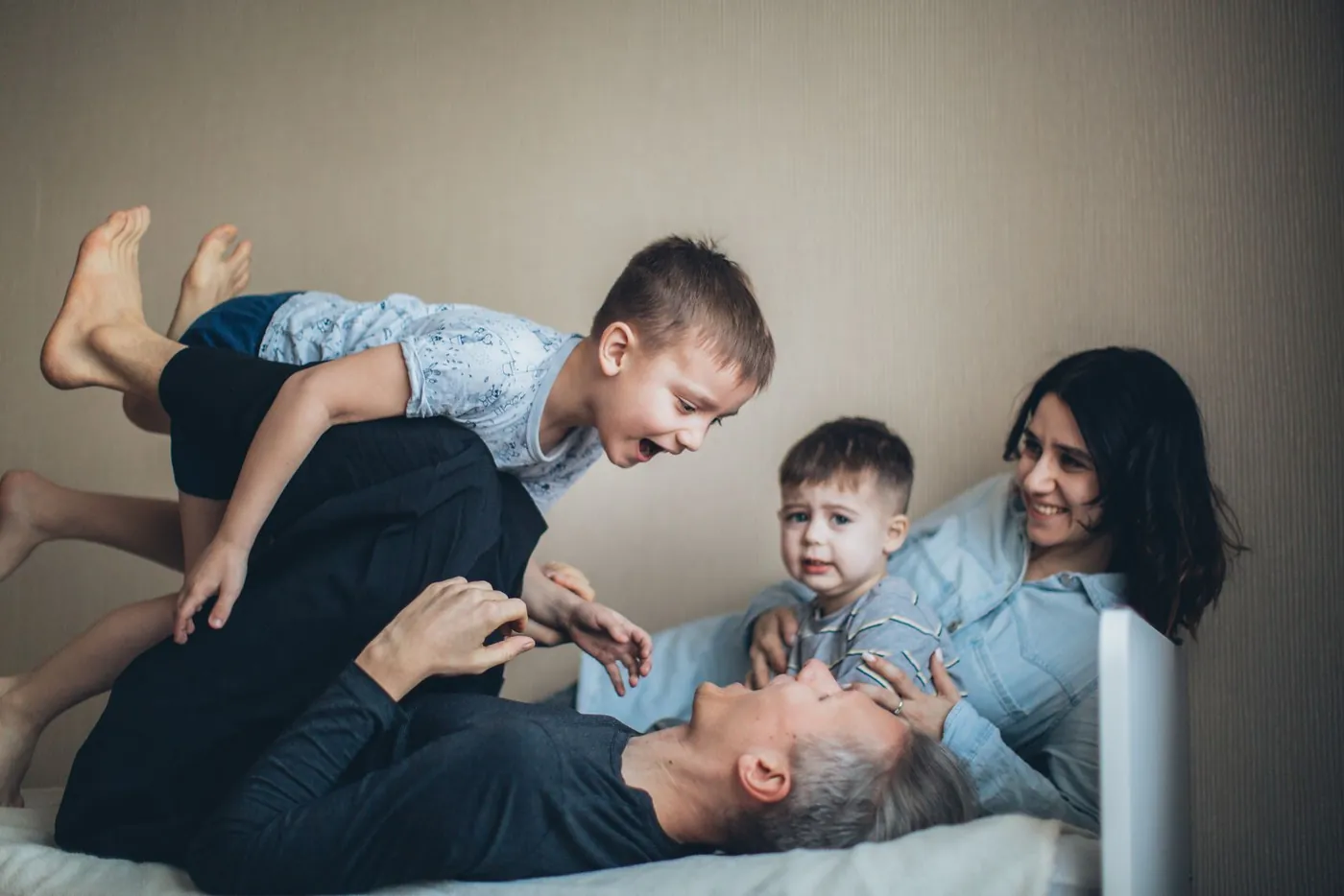 Vater tobt lachend mit zwei Kindern auf dem Bett