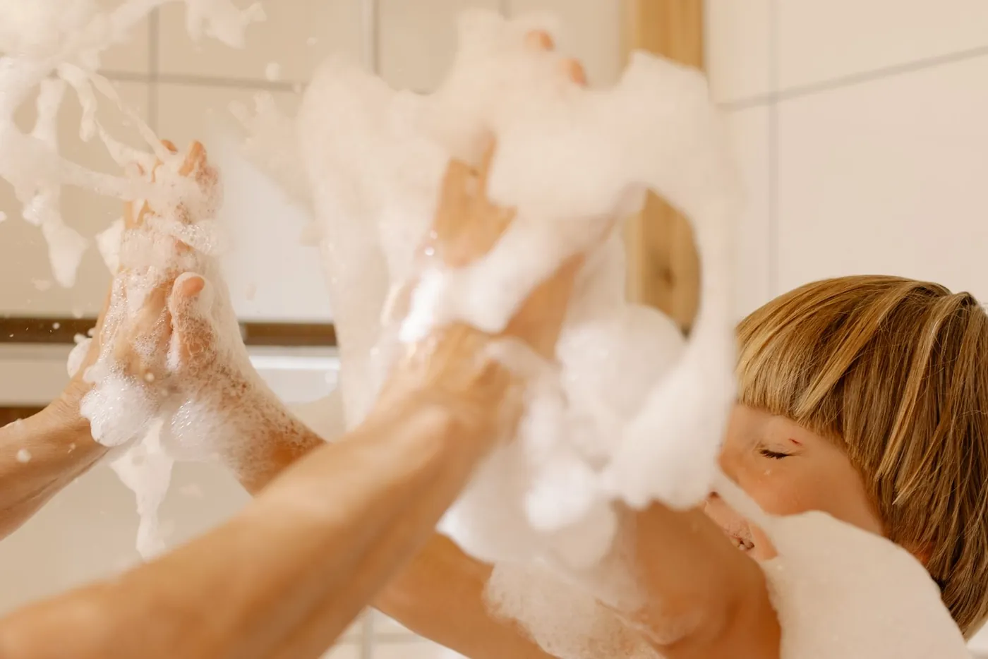 Hände eines Elternteils halten ein Kleinkind beim Baden